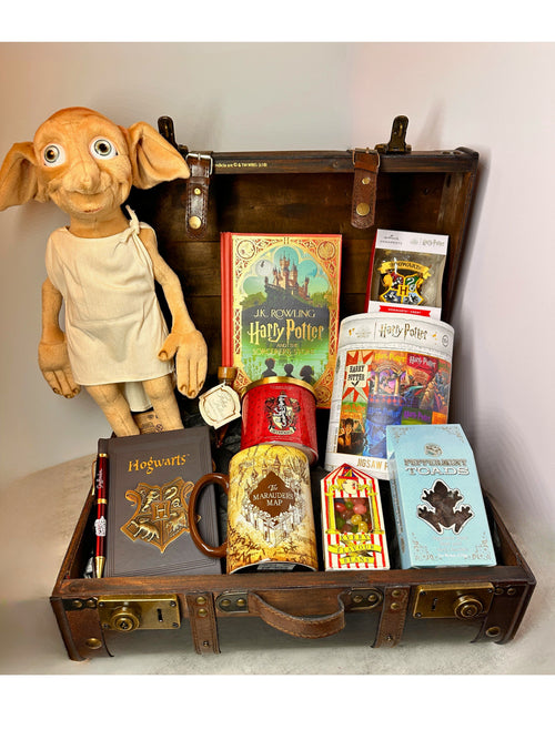 A curated Harry Potter themed gift basket arranged inside an open vintage-style  Harry Potter brown suitcase. Visible items include a Dobby plush figure, a Hogwarts notebook, a Harry Potter book, a Harry Potter themed candle, Harry Potter themed puzzle, Harry Potter Marauders Map mug , Harry Potter Christmas ornament, Harry Potter sweet treats (chocolate frogs, Felix Felicis Liquid Betrtie Bott's)  