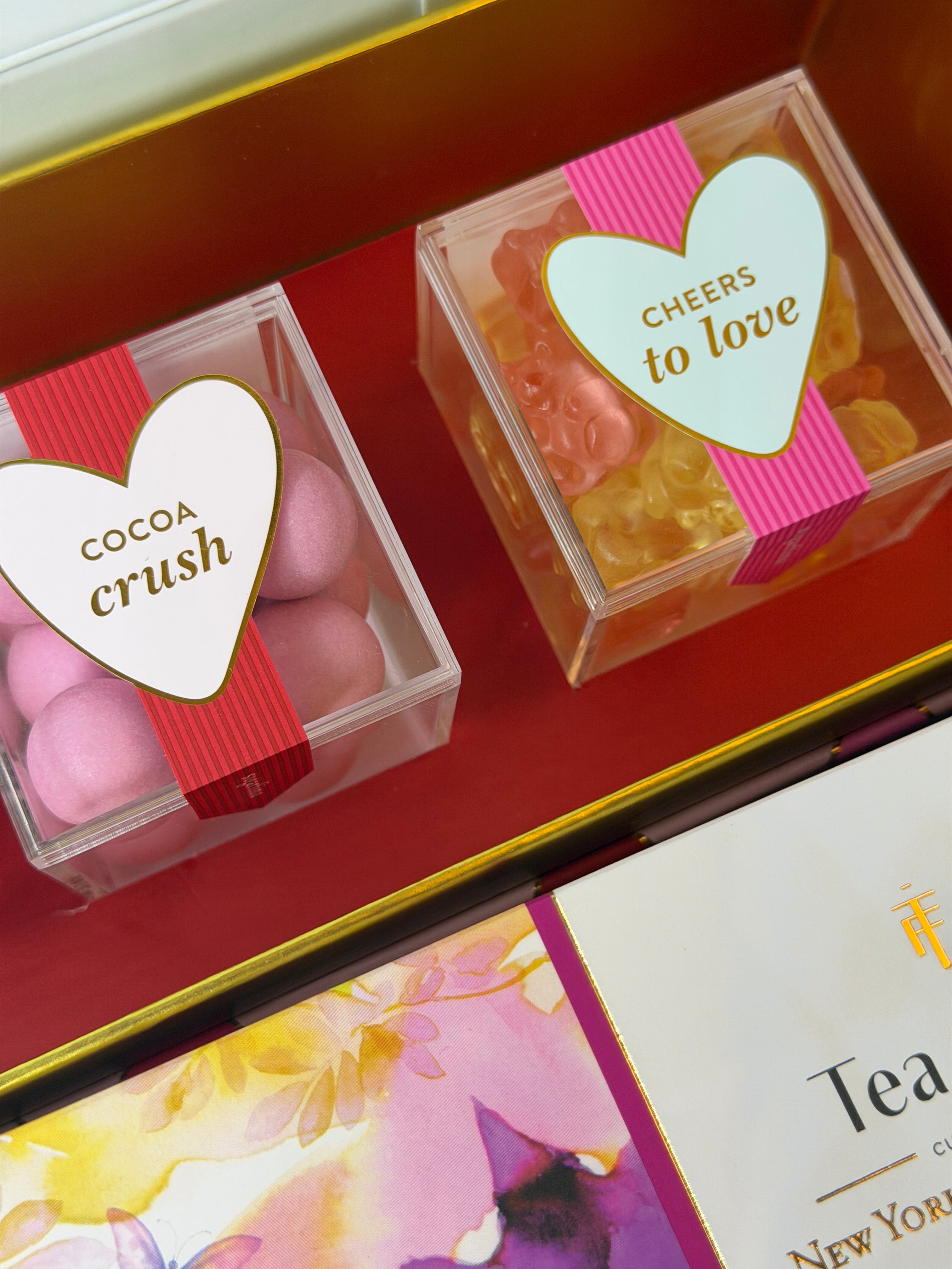 Sugarfina  candy box with heart-shaped labels on a red surface, next to a floral tea box.