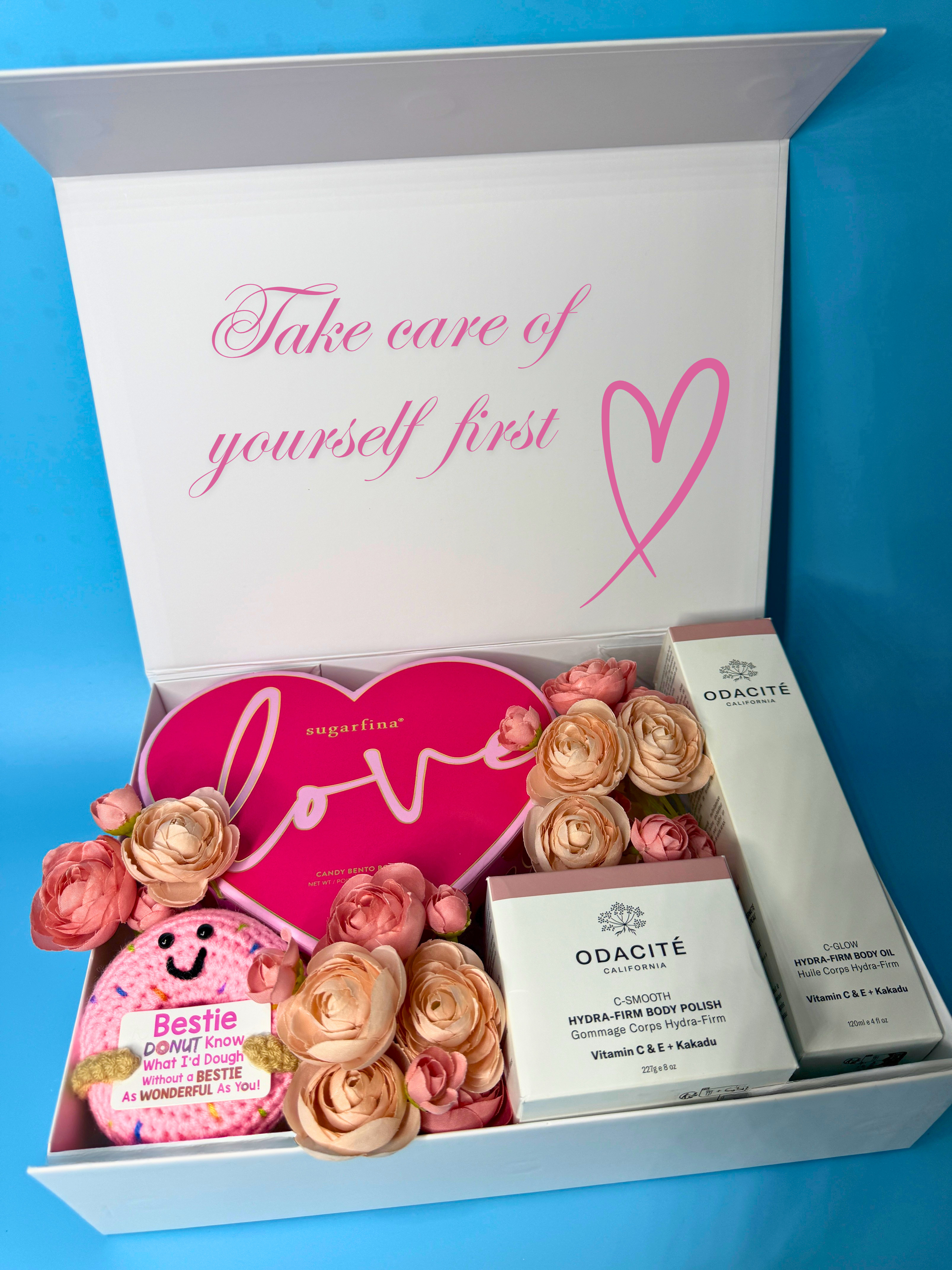 Gift box with a beautiful note on the lid, with flowers, a pink heart candy, and Odacite body care products. 